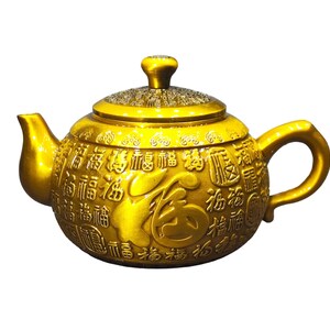 May include: A metallic gold teapot featuring a rounded body and a matching lid. The surface is embossed with numerous repeating Chinese characters, including a large central character, and decorative patterns around the lid and spout.