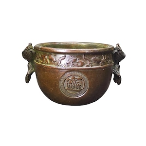 May include: A round bronze-toned metal bowl featuring two fish-shaped handles on the sides. The exterior is decorated with a relief band of lotus flowers and fish, and a central circular medallion containing embossed Chinese characters.