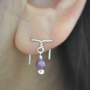 May include: A silver earring with a small purple gemstone dangling from a twisted wire.