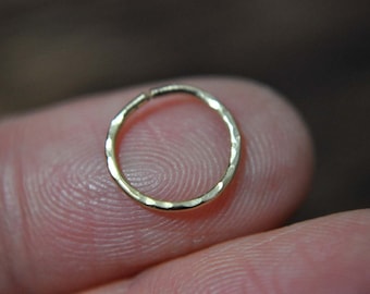 May include: A gold hammered hoop earring, shown on a finger.