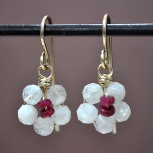 May include: Gold earrings with a cluster of white moonstone beads and red ruby accents. The earrings have a simple wire design.