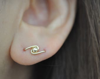 May include: A gold ear cuff with a small ball in the center. The cuff is curved and has a simple design.