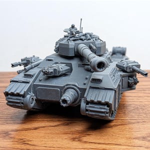 May include: A gray plastic model of a military tank with multiple turrets, cannons, and machine guns. The tank has a detailed design with visible treads and a small figure on top. The model is set on a wooden surface.