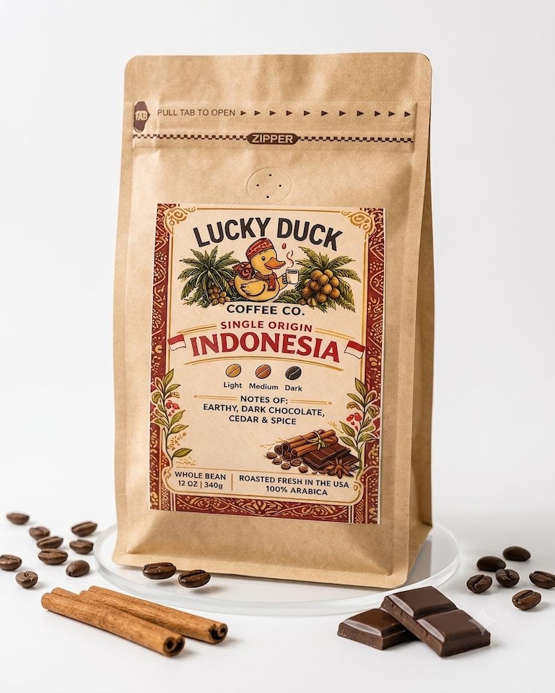 May include: A tan paper coffee bag labeled Lucky Duck Coffee Co. Single Origin Indonesia. The label features a duck illustration, text notes of earthy, dark chocolate, cedar and spice, and states 12 oz | 340g. Coffee beans, cinnamon sticks, and chocolate are nearby.
