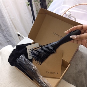 May include: A black hairbrush and a smaller brush are displayed inside a cardboard box. The box also contains a black drawstring bag and a small card. The brand name "ZRHEMA" is printed on the box.