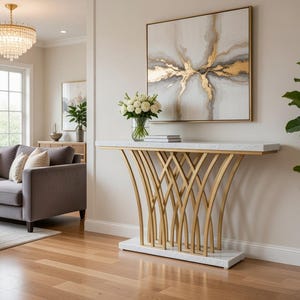 May include: A contemporary living room with a grey sofa, decorative cushions, and a marble-topped console table with a gold base. An abstract painting hangs above the table. A chandelier and a potted plant complete the scene.
