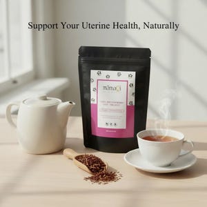 Peut inclure: Une théière en céramique blanche, une tasse de thé et un sachet de thé noir avec une étiquette rose sont disposés sur une surface en bois. L'étiquette indique "Stem Red Raspberry Leaf Organic". Une cuillère en bois contient des feuilles de thé en vrac.