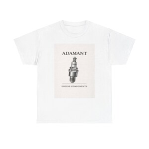 Peut inclure: T-shirt blanc avec un graphique d'une bougie d'allumage, le mot "ADAMANT" au-dessus et "ENGINE COMPONENTS" en dessous. La bougie d'allumage est dans des tons de gris et de noir.