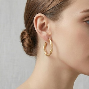 Puede incluir: Una taza de cerámica blanca con un asa negra y el texto "But First, Coffee" en negrita negra. La taza se encuentra sobre un fondo borroso, sugiriendo un ambiente acogedor.