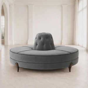 Może przedstawiać: Szara, okrągła sofa z pikowanym oparciem centralnym. Sofa ma ciemne lamówki i drewniane nogi. Design jest nowoczesny i elegancki, odpowiedni do salonu lub strefy wypoczynkowej. Średnica sofy wynosi około 200 cm.