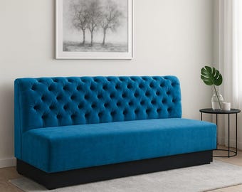 Könnte beinhalten: Ein tuftes, teal-farbenes Sofa mit niedrigem Profil und schwarzem Sockel. Die Rückenlehne des Sofas hat ein Knopf-Tufting-Design. Das Sofa steht vor einer weißen Wand mit einem gerahmten Schwarz-Weiß-Kunstdruck.