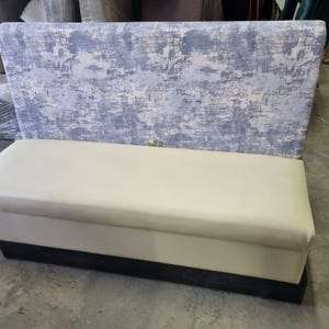May include: A modern bench with a light blue and gray patterned backrest and a cream-colored seat. The base is a dark, solid color. This piece of furniture is suitable for a living room or dining area.