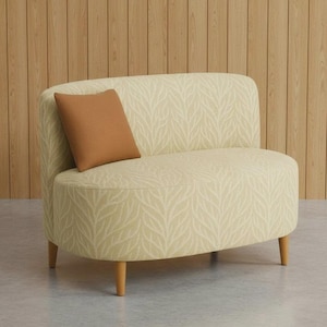 May include: A small, curved sofa with a light yellow leaf pattern fabric. It has a rounded back and two wooden legs. A brown square cushion rests on the seat. The sofa is a stylish piece of furniture.