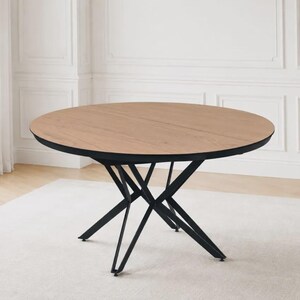 Op de afbeelding: Een ronde eettafel met een lichtbruin houten tafelblad met houtnerf en een zwart metalen onderstel met kruisende, schuine poten die een geometrische steunstructuur vormen onder het ronde oppervlak voor een stabiel meubelstuk.