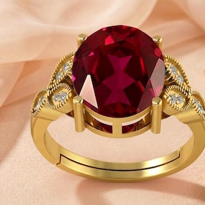 Puede incluir: Un anillo de oro con una gran piedra preciosa de color rojo intenso y corte ovalado, sujeta por cuatro garras. La banda está decorada con pequeñas piedras claras de corte redondo engastadas en motivos metálicos en forma de hoja.
