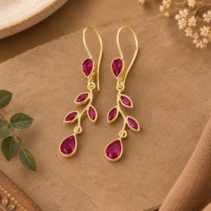 Peut inclure: Une paire de boucles d'oreilles pendantes en or avec un motif de branche orné de plusieurs pierres précieuses rose vif de taille marquise et poire. Les boucles d'oreilles sont suspendues à des crochets simples et présentent des feuilles serties.