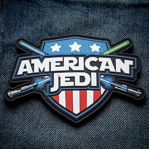 Könnte beinhalten: Ein schildförmiger Aufnäher mit dem Text AMERICAN JEDI in weißen Buchstaben. Das Design umfasst drei weiße Sterne auf blauem Grund, rote und weiße vertikale Streifen sowie zwei gekreuzte, leuchtende Lichtschwerter in Blau und Grün.