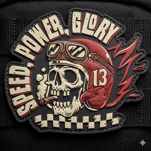 May include: A black, red, and cream-colored patch featuring a skull wearing a red helmet with goggles and the number 13. The text SPEED, POWER, GLORY is arched above, with a cigar in the skull's mouth and a checkered pattern at the bottom.