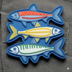 以下が含まれることがあります： 垂直に積み重なった3匹の様式化された魚が描かれた長方形のワッペン。一番上の魚はオレンジ色の縞模様がある水色、真ん中の魚は黄色、一番下の魚は緑色の縞模様がある白色です。すべての魚には青い輪郭線が施されています。