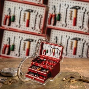 May include: A miniature red tool chest keychain featuring a pegboard back panel with printed tools, three open drawers containing tiny hardware, and the word NAME printed in white on the front. The keychain includes a silver metal ring.