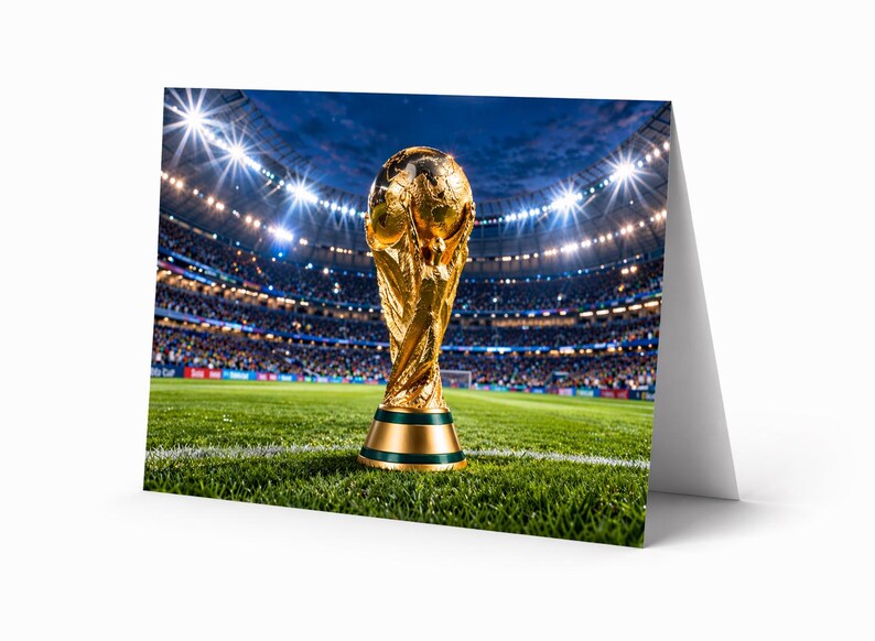 Op de afbeelding: Een wenskaart met de FIFA World Cup-trofee op een groen veld. De gouden trofee staat op de voorgrond, met op de achtergrond een stadion vol toeschouwers en heldere lichten. De kaart is wit.