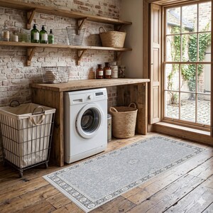 May include: A laundry room with a white washing machine, wooden shelves, and a light gray rug with a floral pattern. The room has a brick wall and a window with a view of greenery. Baskets and cleaning supplies are visible.