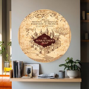 May include: A round, vintage-style wall art piece featuring a map design. The map is in shades of brown and beige, with text that reads "The Marauder's Map." The artwork includes a castle illustration and decorative borders.
