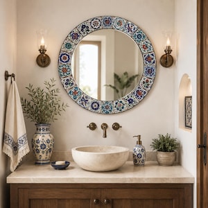May include: A round wall mirror featuring a decorative frame composed of colorful floral patterned tiles in shades of blue, red, and green. The mirror is positioned above a stone vessel sink, a matching ceramic vase, and a soap dispenser.