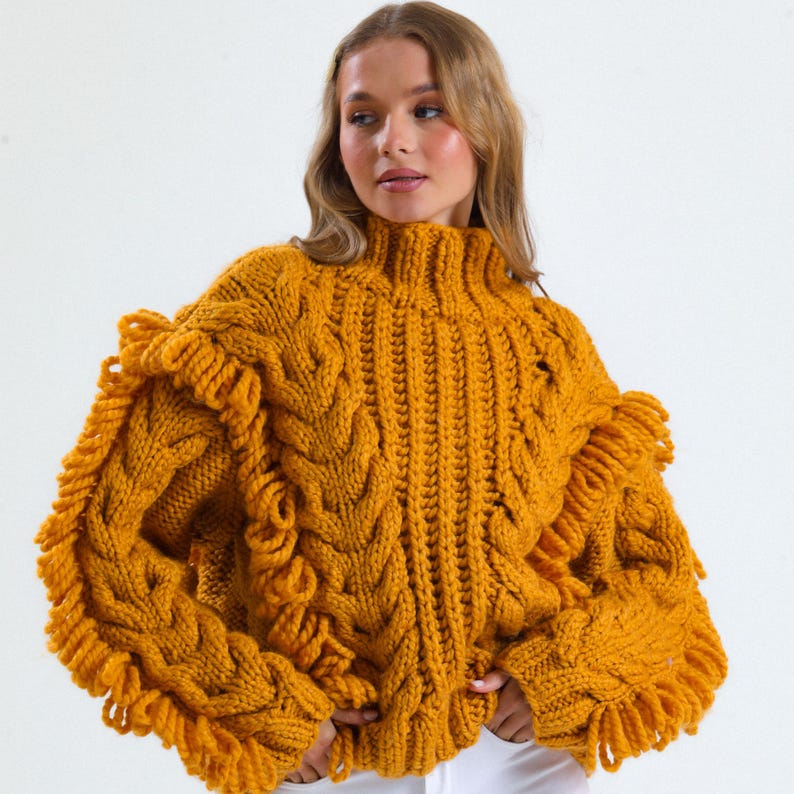 Pode incluir: Camisola de malha canelada amarelo mostarda com gola alta e mangas com franjas. A malha grossa apresenta um padr&atilde;o texturizado e um ajuste descontra&iacute;do. A camisola &eacute; uma pe&ccedil;a de roupa quente e aconchegante.