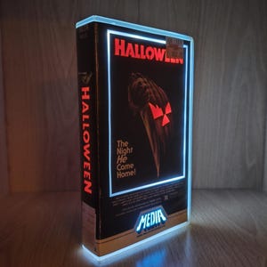 May include: A rectangular, illuminated display case shaped like a vintage Halloween VHS tape. The front features the movie title, a graphic of a hand holding a knife, and the text The Night He Came Home. The Media logo is at the bottom.
