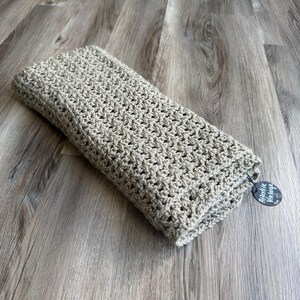 May include: A rectangular, beige crocheted textile featuring a consistent, repeating open-work stitch pattern. A small, circular black tag with the white text Afterlike Vintage is attached to one corner of the folded fabric with a thin black cord.