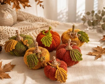 Pode incluir: Uma coleção de seis pequenas abóboras redondas tricotadas à mão em cores de outono, incluindo verde-azeitona, laranja queimado e amarelo-dourado. Cada abóbora apresenta uma superfície canelada, um caule castanho e uma folha verde em croché.