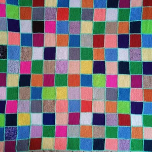 Puede incluir: Una manta tejida que presenta una cuadrícula de parches cuadrados multicolores. Los cuadrados están dispuestos en un patrón repetitivo de varios colores, incluyendo rojo, azul, verde, amarillo, naranja, rosa, morado, gris y marrón, unidos por un hilo fino de color verde azulado.