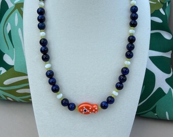 Collar con cuentas de ojo de tigre azul, dije de pez y detalle de perla.