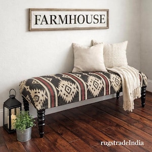 May include: A farmhouse-style bench with a patterned fabric seat in black, cream, and red. The bench has turned black legs and is adorned with cream-colored pillows and a fringed throw. A framed sign that reads "FARMHOUSE" hangs above.