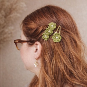 Peut inclure: Des pinces à cheveux à fleurs en crochet vert avec des perles sont présentées dans des cheveux auburn. Une barrette dorée maintient une seule fleur. Accessoires de cheveux faits à la main.