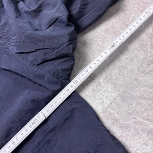 May include: Dark navy blue fabric, possibly clothing, with a wrinkled texture. A white ruler with black markings is placed diagonally across the fabric, showing measurements from 52 to 91 inches.