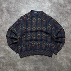 Könnte beinhalten: Ein langärmeliger Pullover mit Rundhalsausschnitt und einem sich wiederholenden geometrischen Muster in Dunkelblau, Waldgrün und gedecktem Rot. Das Kleidungsstück hat einen gerippten Kragen, Bündchen und Saum sowie ein kleines blaues Etikett.