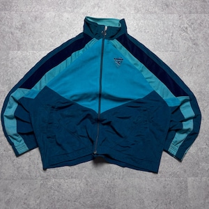 May include: A vintage teal and blue track jacket with a full zip and a high collar. The jacket has a colour-blocked design with navy blue and teal accents. A small logo is visible on the chest.