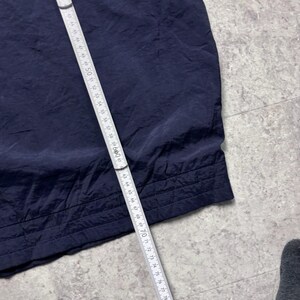 May include: A navy blue fabric, possibly clothing, is measured with a white and silver measuring tape. The tape shows measurements up to 84 inches. The fabric has a textured appearance and a stitched hem.