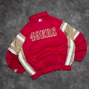 May include: A red Starter brand jacket featuring the text 49ERS in white and gold lettering on the back. The jacket has gold and white side panels, a high collar, and a Starter logo on the upper back and the sleeve cuff, with a full-length front zipper.