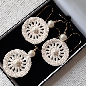 May include: Three pairs of crocheted earrings with pearl accents. The earrings are white and have a delicate, intricate design. They are displayed in a black box.