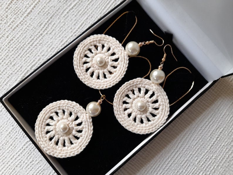 May include: Three pairs of crocheted earrings with pearl accents. The earrings are white and have a delicate, intricate design. They are displayed in a black box.