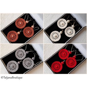 May include: Four pairs of crocheted earrings in different colors. The earrings are displayed in black boxes. The colors are red, white, gray, and orange.