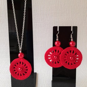 May include: Red crocheted earrings and necklace set with silver chain and red beads. The earrings and necklace feature a circular design with a red bead in the center.