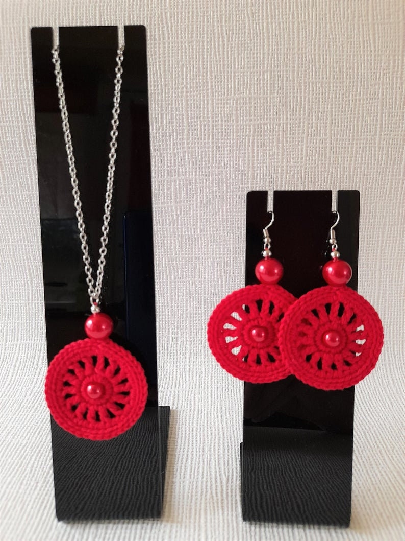 May include: Red crocheted earrings and necklace set with silver chain and red beads. The earrings and necklace feature a circular design with a red bead in the center.