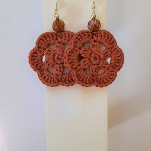 May include: A pair of crocheted earrings with a brown flower design and brown crystal beads.