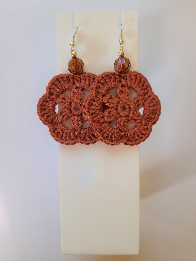 May include: A pair of crocheted earrings with a brown flower design and brown crystal beads.