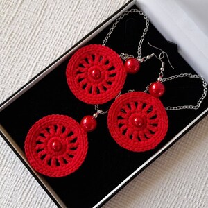 May include: A set of red crocheted earrings and a necklace with red beads. The jewelry is displayed in a black box.