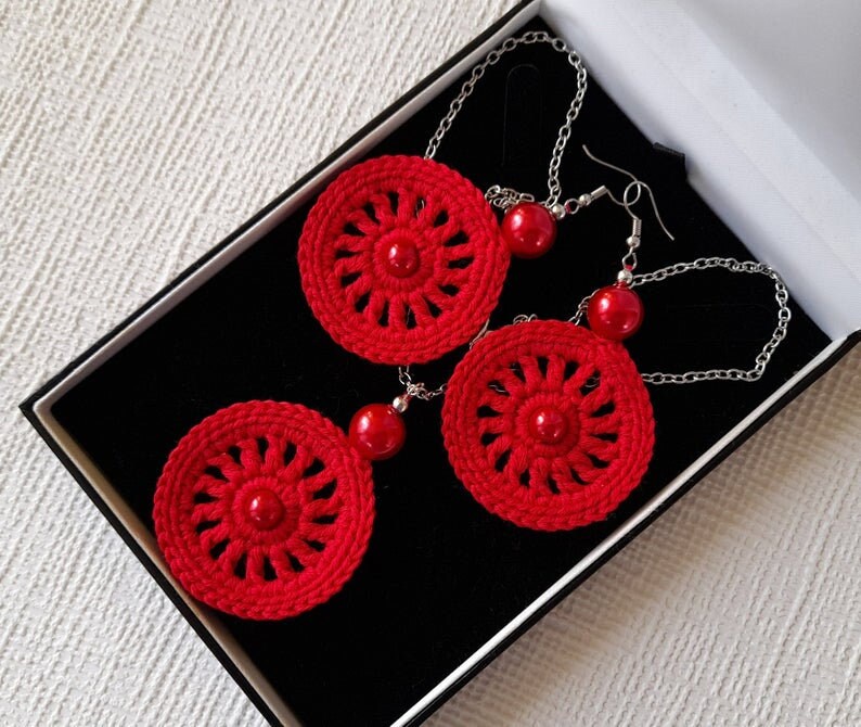 May include: A set of red crocheted earrings and a necklace with red beads. The jewelry is displayed in a black box.